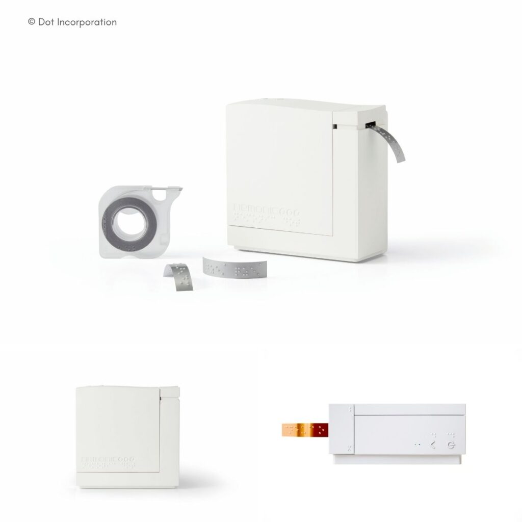 Dot Incorporation Braille-Drucker in Weiß mit austretendem Metallband, dazu Zubehör: Bandrolle, Kassette und Druckereinheit mit Braille-Ausgabe.