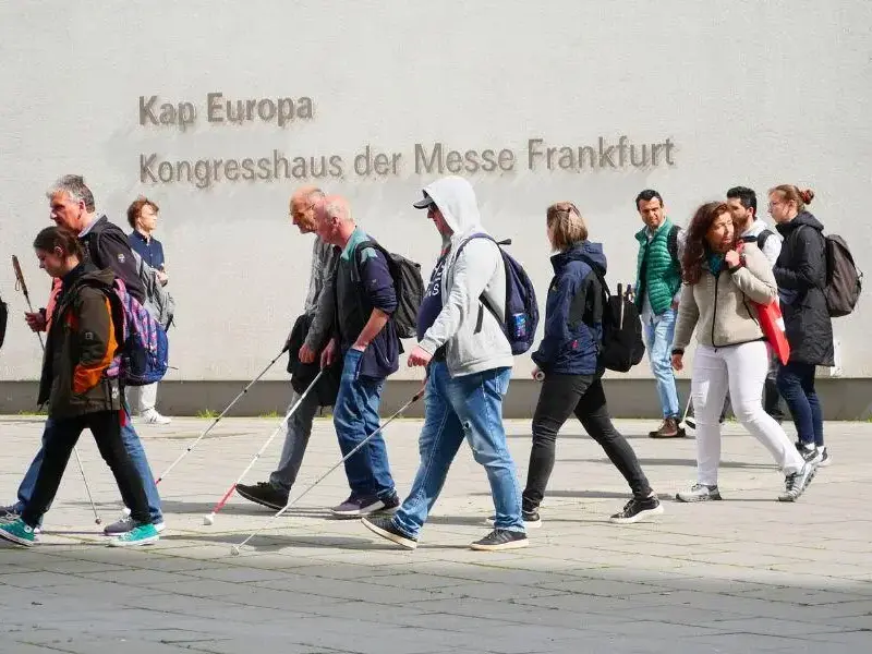 Menschen, zum Teil mit Blindenstock laufen an weißem Gebäude mit der Aufschrift Kap Europa vorbei