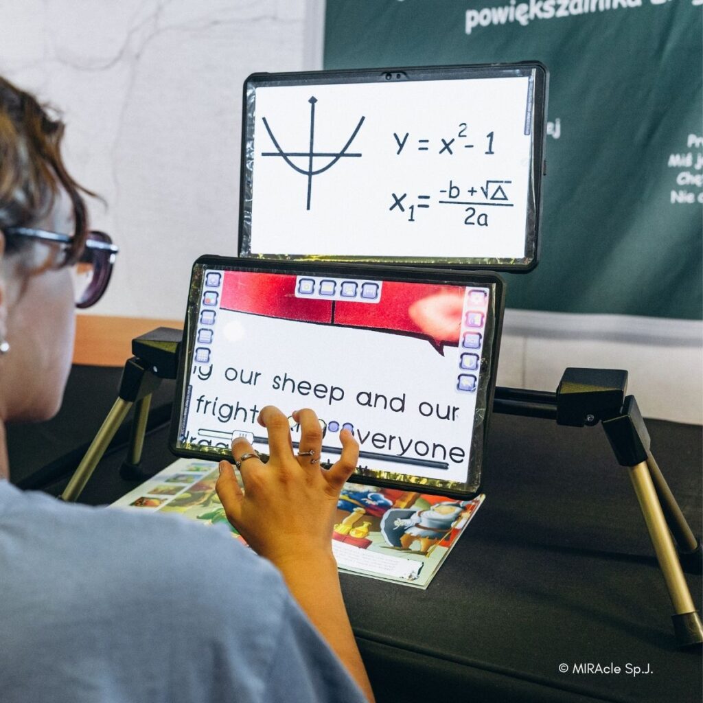 Schülerin mit Brille nutzt zwei MIRAcle-Bildschirmlesegeräte: oben eine Mathematikaufgabe, unten stark vergrößerter Text. Im Hintergrund eine Schultafel.