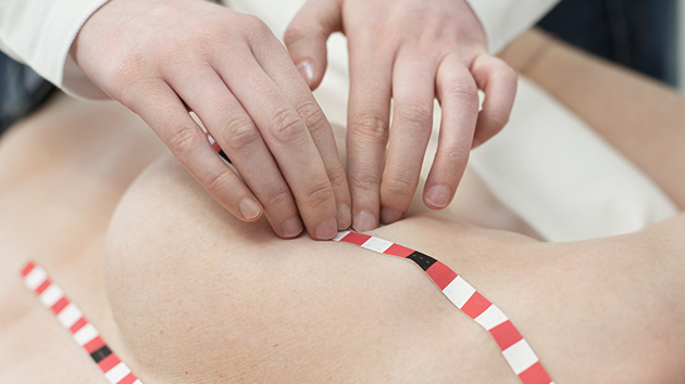the hands of an MTE examine a female breast, marked with tactile orientation strips