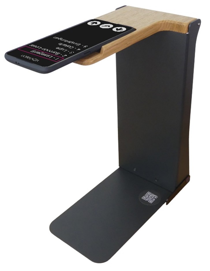 A reading device that looks like a smartphone, positioned in a reading stand. The stand is made of black metal and wood.